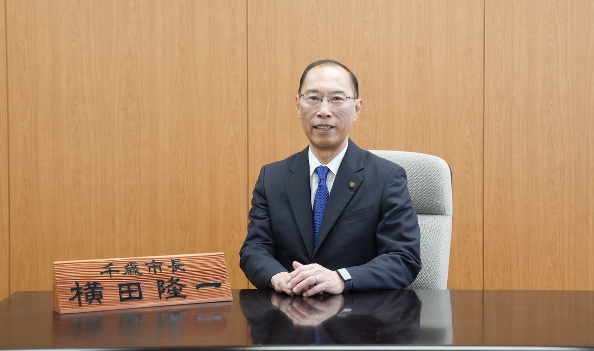 正面を向いて座る千歳市長・横田隆一の 肖像写真。手前に木製ネームプレー トが置かれている。