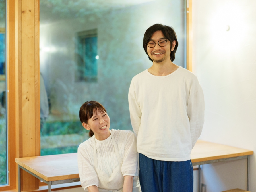 笑顔で窓辺に並ぶ小椋夫妻の写真