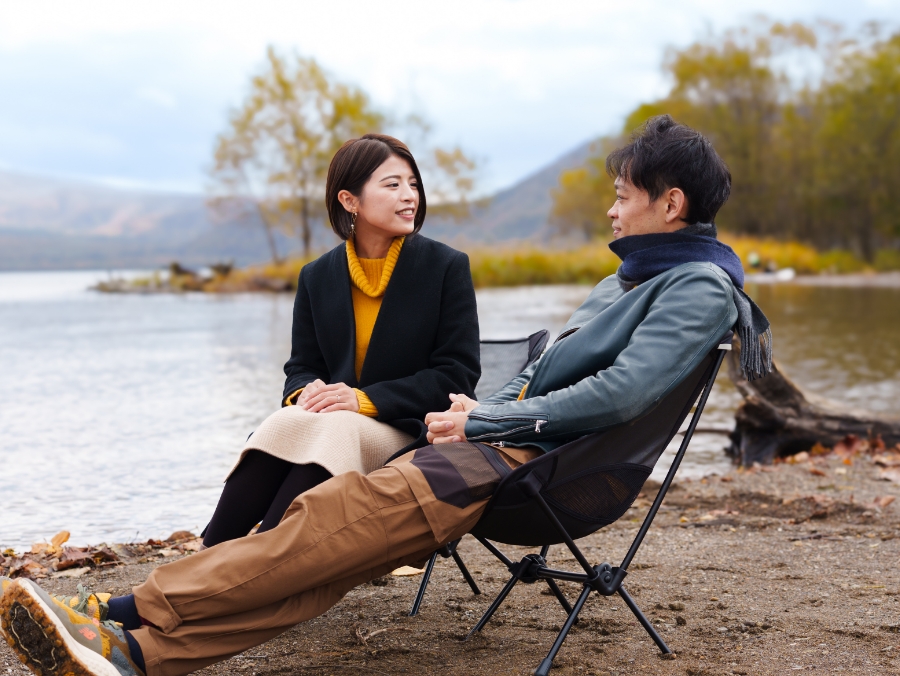 秋の支笏湖畔で椅子に座りながら会話を楽しむ二人の写真